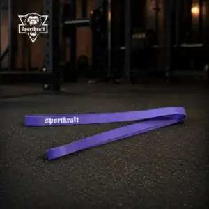 Pitkä violetti SportKraft Light vastuskuminauha asetettuna kuntosalin lattialle levytankotelineiden eteen.