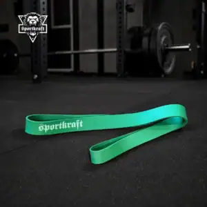 Vihreä pitkä SportKraft Average vastuskuminauha kuntosalilla levytangon ja voimanostotelineen yhteydessä.